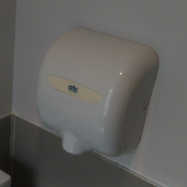 A smooth white ATC hand dryer attached to a plain white wall in a modern restroom
