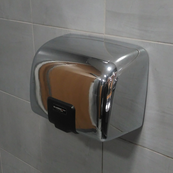 A hench silver Classic MKII Airdri Hand Dryer attached to a grey tiled wall in a service station restroom