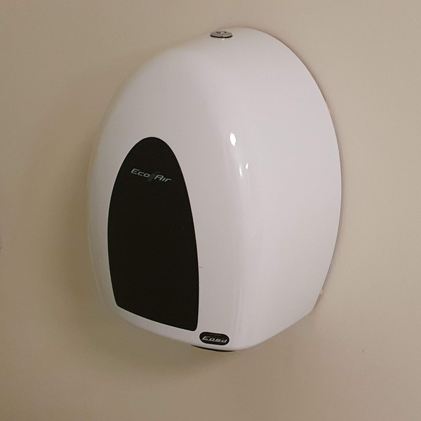 A slim pod-like white Eco Air Hand Dryer attached to a cream-coloured wall in a retro restroom